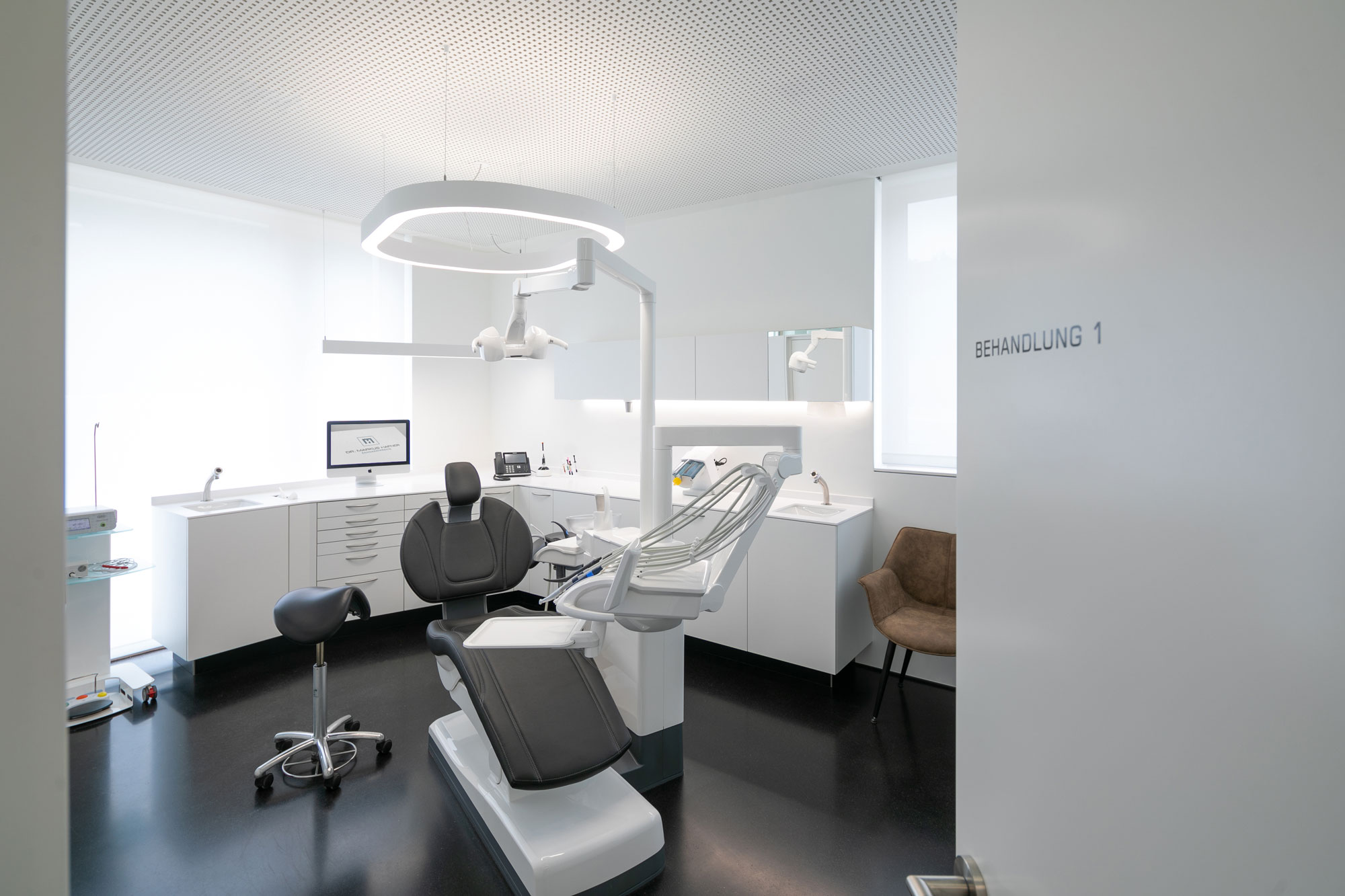 A slim, white pendant light provides precise, glare-free light in the treatment room of a dental practice.